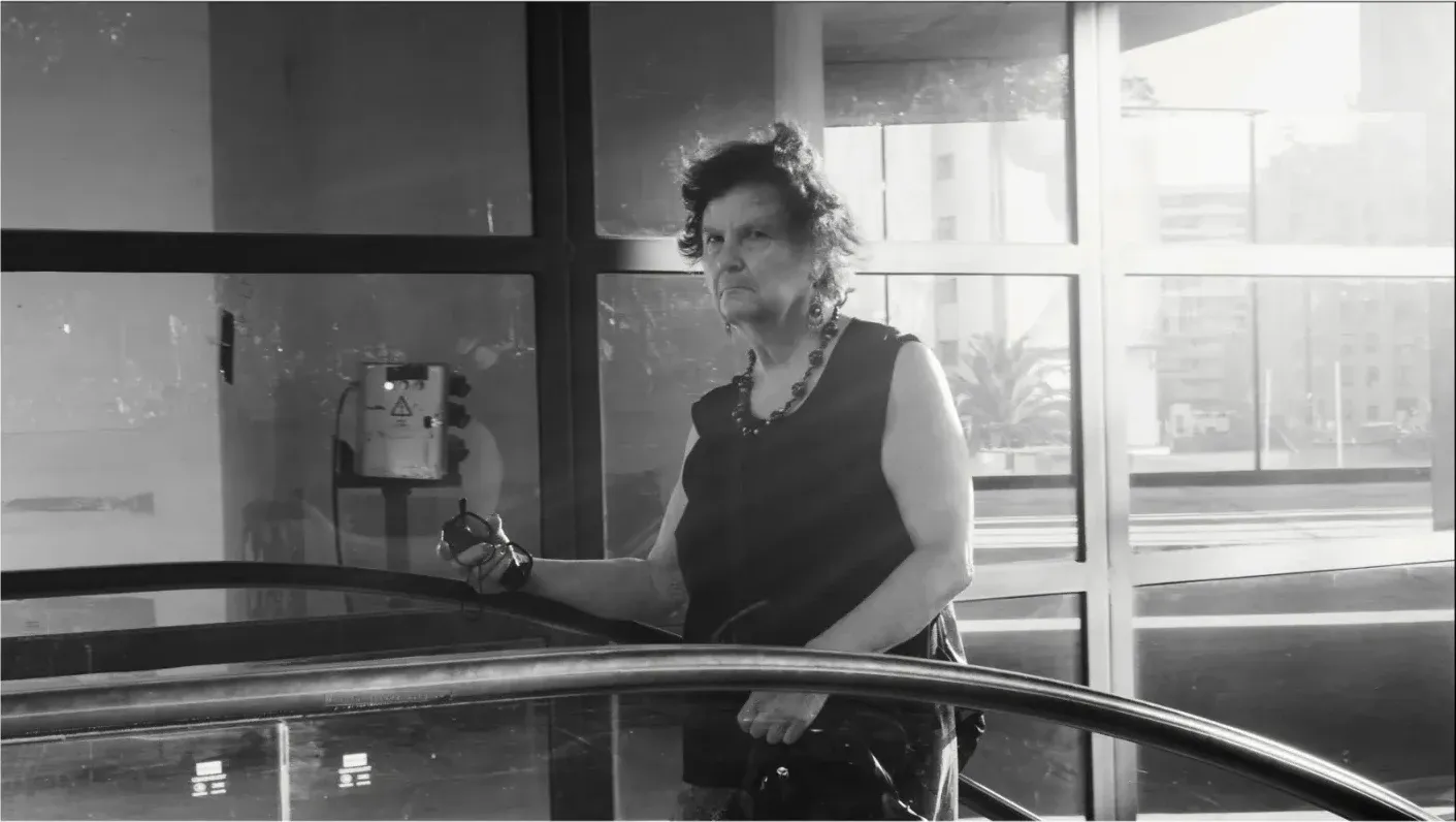 Mujer mirando a cámara desde una escalera mecánica, en blanco y negro
