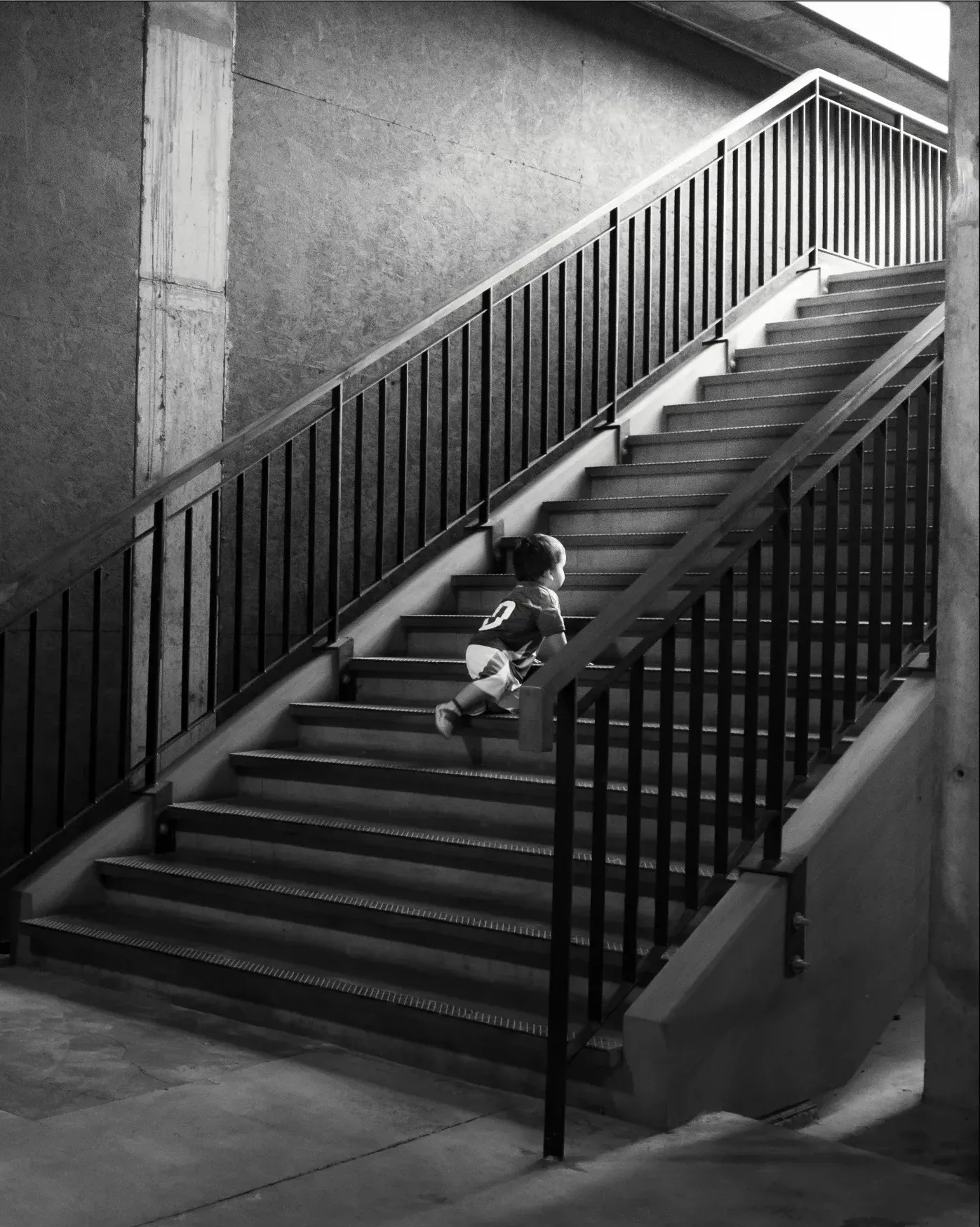Niño subiendo una larga escalera de concreto, en blanco y negro